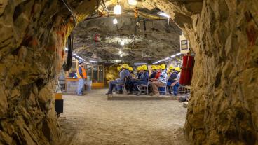Students wearing yellow hard hats sitting at desks in the classroom in Edgar Mine. A professor in a blue hard hat faces them at the front of the room.