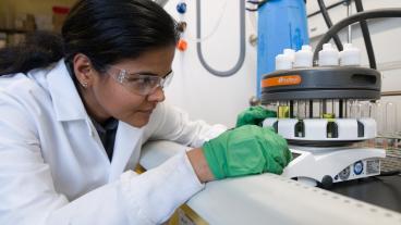 ramya kumar in lab coat and green gloves working in lab
