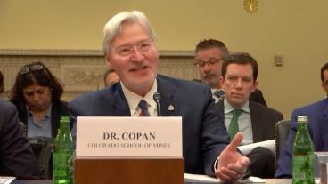 Walt Copan sits at witness stand with people taking notes behind him