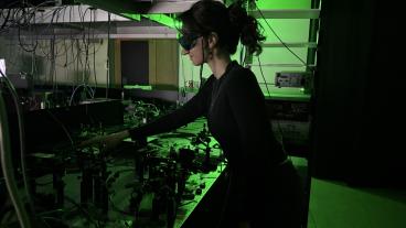 female student in all black working in lab lit by green light