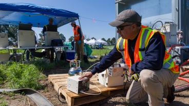 man kneels in front of air testing equipment outside
