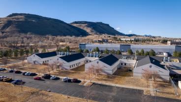 aerial photo of white building with dark roof and four wings and mountains in background