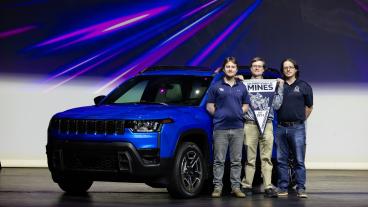 three men holding Mines pennant stand in front of blue Jeep Cherokee