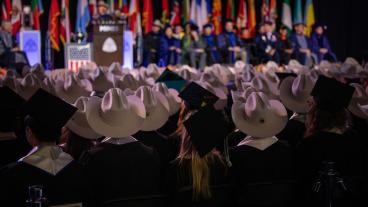 graduates in a mix of cowboy hats and mortarboards sit in front of commencement stage