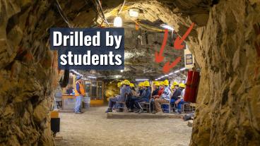 Students wearing hard hats sit in an underground classroom during a tour of the Edgar Experimental Mine, with text reading “Drilled by students” and arrows pointing to mine features.