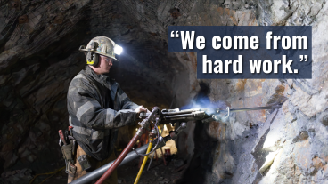 Student wearing a hard hat operates drilling equipment inside a mine, with on-screen text that reads, “We come from hard work.”