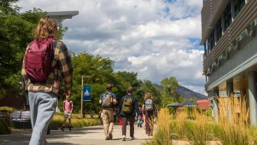 student wearing backpack walks down pedestrian sidewalk with more students walking ahead