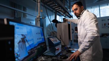 researcher in white lab coat in front of computer monitor with figures on the screen