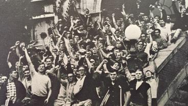 Black and white photo of the 1966 freshman class as they celebrate in front of one of the building on the Mines campus