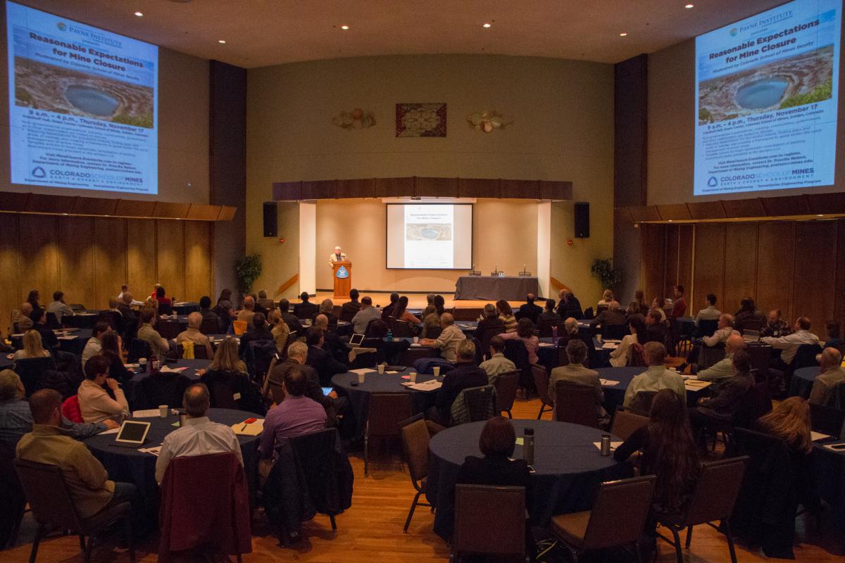 A full room of people watching a powerpoint presentation about mine remediation